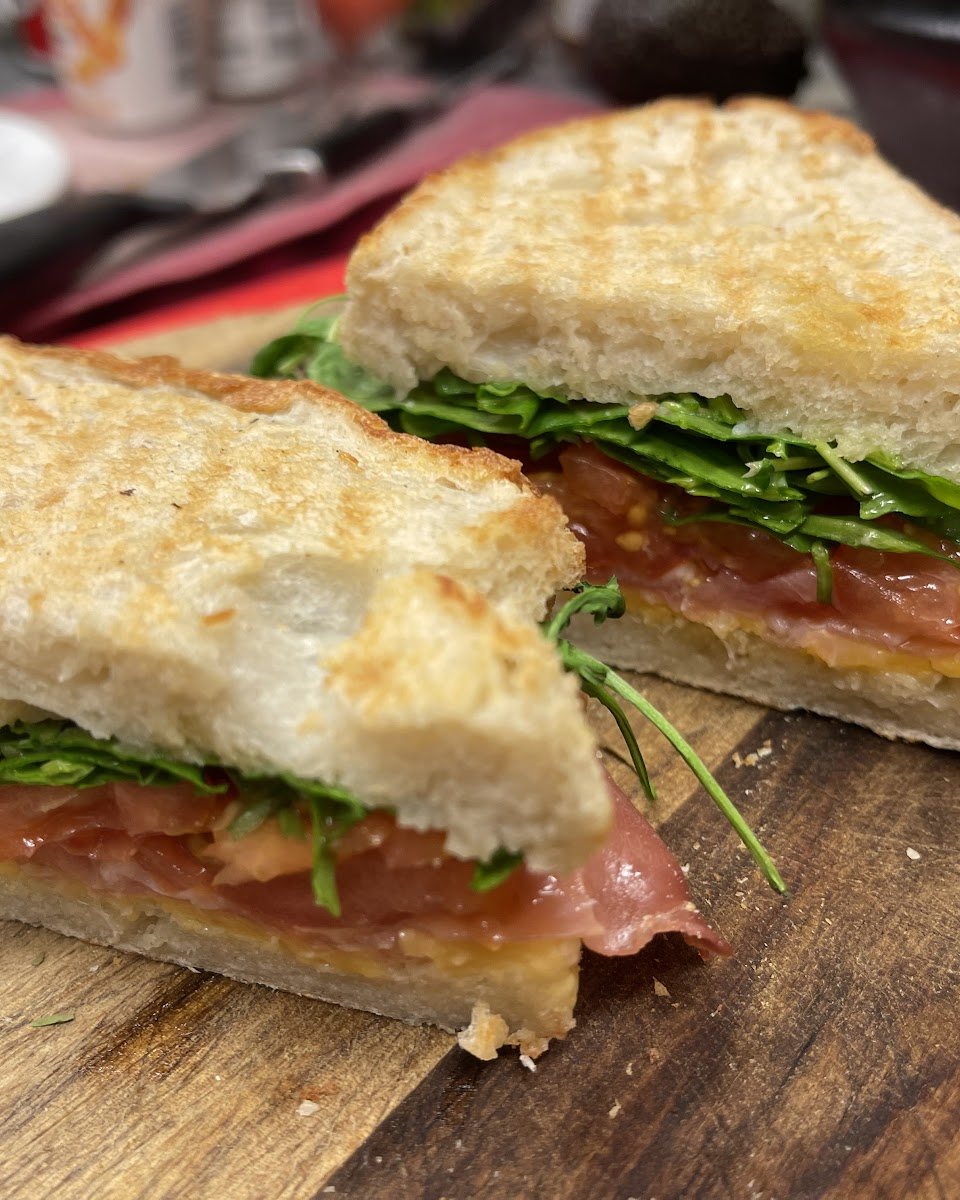 A toasted sandwich with prosciutto, rocket and tomato, cut in half, at Nico's